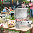 A DirectDeals Stainless Steel Propane Grill with Lid for Outdoor Camping Tailgating Picnic Party-Silver sits on a picnic table with smoked food, fruit, and flowers as people enjoy a backyard barbecue.