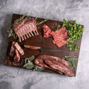 Raw cuts of beef and lamb with herbs, the Steelport Knife Co. 6" Boning Knife, and sea salt are arranged on a dark cutting board atop a gray surface, showcasing the artistry of precision meat cutting with this handcrafted-in-USA blade from Steelport Knife Co.