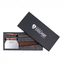 A Steelport Knife Co. 3-Piece Baker Set gift box, partially open, reveals three handcrafted kitchen tools with wooden handles nestled inside a black foam insert. The box lid displays the Steelport Knife Co. logo and company name in white text.