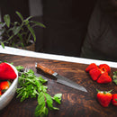 The Steelport Knife Co. 4" Paring Knife rests on a wooden cutting board surrounded by fresh mint leaves and strawberries, with additional herbs and part of a white bowl of strawberries nearby.