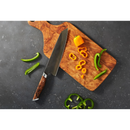 A wooden cutting board with the Steelport Knife Co. 8" Chef Knife—celebrated for its exceptional blade edge retention—rests beside sliced yellow and green peppers, whole green chilies, and a whole mini yellow bell pepper on a dark countertop.