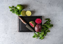 A Steelport Knife Co. Bar Set paring knife is placed on a mini cutting board alongside halved prickly pears, fresh mint leaves, a whole lime, and two lime halves, all arranged on a light stone surface.
