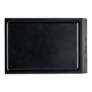 A rectangular black cutting board with a groove around the edge, featuring a wooden section on one end engraved with the Steelport Knife Co. logo—perfect to use as a mini cutting board for preparing garnishes or pairing perfectly with your favorite paring knife from the Steelport Knife Co. Bar Set.