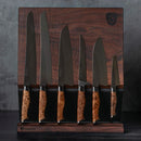 The Steelport Knife Co. Full Kitchen Set, featuring six American-made knives with wooden handles, is shown standing upright on a dark wooden magnetic knife block against a gray background.
