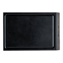 A rectangular black portable cutting board with a raised edge and a walnut wood section on one side, featuring the Steelport Knife Co. brand engraved on the wood. The elegant end-grain walnut accent adds both durability and style to this versatile kitchen essential—the Steelport Knife Co. SteelCore™ 2-in-1 Walnut Cutting Board, measuring 9"x6".