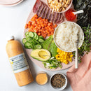 A platter with sushi rice, seared tuna, diced salmon, grilled chicken, cucumber, avocado, mango, scallions, seaweed, sprouts, roe, sesame seeds, a bowl of sauce and Terrapin Ridge Farms Zesty Seven Spice Dressing.