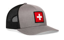 The Haka Hat Swiss Flag Trucker Hat by Haka Hat is a gray and black mesh snapback featuring a bold red patch with a white cross on the front, blending classic style with Swiss heritage.