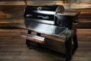 Recteq RT-800 / Deck Boss 800 featuring a Pimp My Grill® Tactical Stainless Folding Front Shelf with an attached butcher paper dispenser, serving as a convenient grill prep workspace.