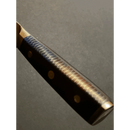 Close-up of the Spaceman Knives Interstellar Kiritsuke Knife handle, featuring a textured wave-like pattern and three brass rivets, set against a dark background.