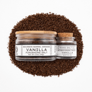 Two jars of Texas Salt Co. Bourbon Barrel Smoked Vanilla Finishing Salt, in large and small sizes with clear labels and wooden lids, sit on a mound of dark brown salt against a crisp white background.