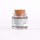A 1oz glass jar of Texas Salt Co. Chile Lime Smoked Salt with a cork lid, vibrant seasoning inside, and labeled with the Texas Salt Co brand, is shown against a white background.