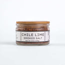 A small glass jar with a wooden lid holds Texas Salt Co. Chile Lime Smoked Salt, 4.5oz (128g). The white label highlights this zesty twist on classic smoked salt by Texas Salt Co.