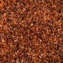 Close-up of coarse brown and reddish Texas Salt Co. Chile Lime Smoked Salt crystals, showing varied sizes and shades packed tightly to form a richly textured surface.