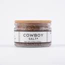 A clear glass jar with a wooden lid labeled Texas Salt Co. Cowboy Salt® holds 3.75 oz (106g) of Texas finishing salt. The white label has black text and a minimal design, shown on a plain white background.