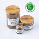 Three glass jars of Texas Salt Co. Cowboy Salt® finishing salt, each with a wooden lid and white label, are displayed under a green International Flavor Awards badge. The jars vary in size and show the Texas Salt Co brand name.
