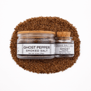 Two jars of Texas Salt Co. Ghost Pepper Smoked Salt, one large and one small, sit on a pile of coarse brown salt. The glass jars have white labels with black text and are topped with cork and wooden lids. Brand: Texas Salt Co.