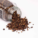 A Texas Salt Co. Thick Hickory Smoked Peppercorn glass jar lies on its side, spilling peppercorn pieces onto a white surface.