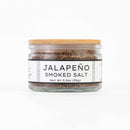 A glass jar with a wooden lid holds Texas Salt Co. Jalapeño Smoked Salt, Net Wt 3.5oz (99g); the label shows the product and brand name, and the jar is displayed against a white background.