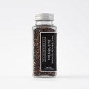 A clear glass jar with a silver lid contains dark smoked black peppercorns. The black label says Texas Salt Co. Mesquite Smoked Peppercorn, a bold Texas seasoning, net weight 4.5 oz (128g), set against a plain white background.