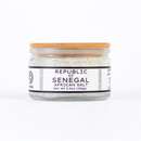 A clear glass jar with a wooden lid, labeled Texas Salt Co. Republic of Senegal African Salt, Net Wt 5.5oz (156g), containing coarse, mineral-rich sea salt crystals. The white label features black text.