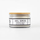A glass jar with a wooden lid labeled Texas Salt Co. Sel Gris French Salt, Net Wt 4.5oz (128g), on a white background. The jar contains coarse, mineral-rich French sea salt from Texas Salt Co.