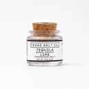 A small glass jar with a cork lid labeled Texas Salt Co. Tequila Barrel Smoked Lime Finishing Salt (.5oz/14g) features citrusy, tequila barrel smoked lime salt from Texas Salt Co., displayed on a plain white background.