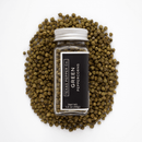 A glass jar labeled Texas Salt Co. Green Peppercorn sits upright on a pile of whole green peppercorns, their fresh citrus aroma apparent against a white background. The net weight is 1.5 oz (43g).