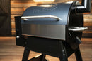 A Pimp My Grill® Bodyguard Stainless Steel Grease & Paint Protector installed on the front of a black pellet grill lid to protect the paint.