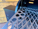 A Pimp My Grill® Pro Series Slide-Out Rack System for Traeger Tailgater / Junior, featuring a metal grill rack with a diamond-patterned grate and circular cutouts, partially pulled from a pellet grill.