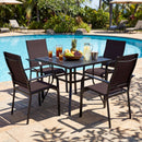 The 5 Pieces Patio Dining Set for 4 Outdoor Square Table and Stackable Chairs by DirectDeals is arranged poolside, with fruit, a pineapple, iced tea, lemonade on the table, surrounded by green plants and lounge chairs.
