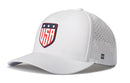 Introducing the Haka Hat USA Shield Performance 5-Panel Hat | America Flexfit Snapback, a white performance hat by Haka Hat featuring a shield-shaped USA logo with three stars above the letters on the front. Designed for comfort and durability, it includes small ventilation holes on the sides and is finished with a subtle H logo. The water repellent construction and Flexfit sweatband help keep you cool and dry all day long.