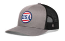 The Haka Hat USA Stripes Trucker Hat | Black America Snapback by Haka Hat features a gray and black mesh design with a circular blue, red, and white logo on the front and a small square logo on the mesh side panel, capturing classic patriotic style in an America snapback.