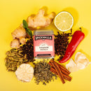 A tin of Spicewalla Tandoori Masala by Spicewalla, the perfect Indian spice blend for grilled chicken, sits among fresh ginger, a halved lemon, red chili pepper, garlic, cloves, cardamom pods, cinnamon sticks, herbs, and black peppercorns.