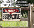 Vintage-style 'Warning BBQ Zone' sign on a wooden fence with grass and flowers in the background.