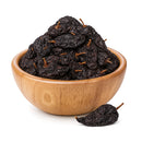 A wooden bowl filled with Rico Rico Ancho Dried Chiles – Sweet & Smoky Mexican Peppers (Mild Heat) by Rico Rico, featuring one dried chile placed outside the bowl on a white background—perfect for adding authentic Mexican flavor to your dishes.