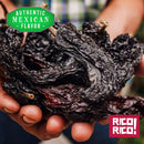 A person holds Rico Rico Chipotle Morita Chile Powder Shaker in their hands, highlighting the essence of authentic Mexican cuisine. A green label reads "Authentic Mexican Flavor," while a red Rico Rico logo appears in the corner, promising a smoky and savory flavor reminiscent of chipotle powder.