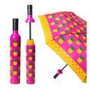The Vinrella Pineapple Punch Bottle Umbrella features a pink canopy with yellow pineapples. Shown open and closed, it fits in a matching, bottle-shaped case for a playful, coordinated tropical style.